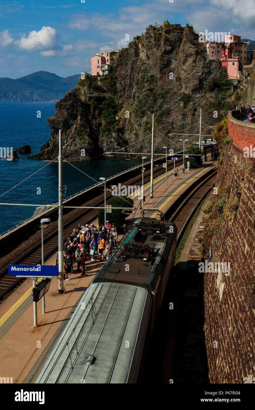 Overhead view of train arriving in Manarola station with waiting tourists and cliffside homes Stock Photo