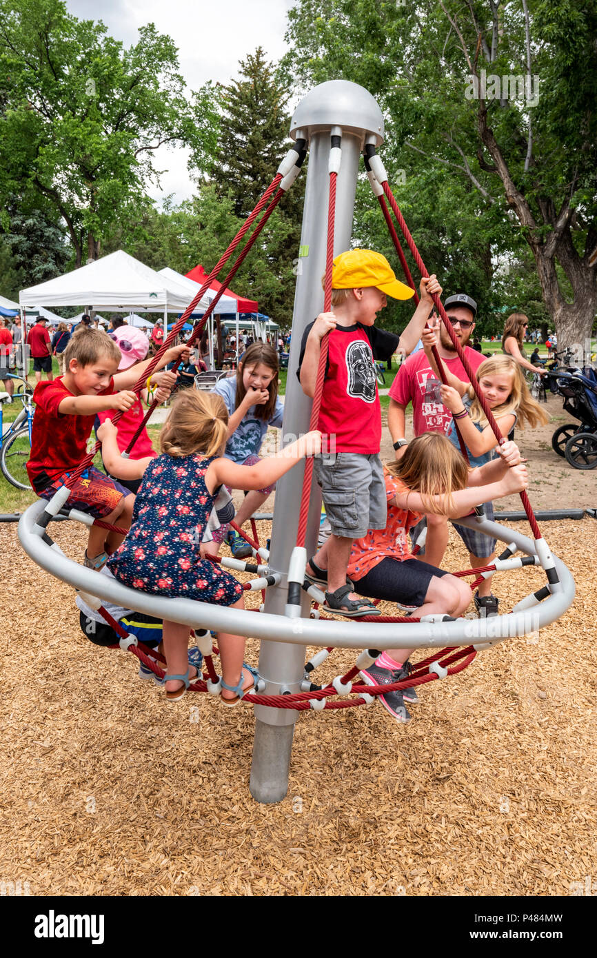 Young children spinning on playground merry-go-round; Salida; Colorado; USA Stock Photo