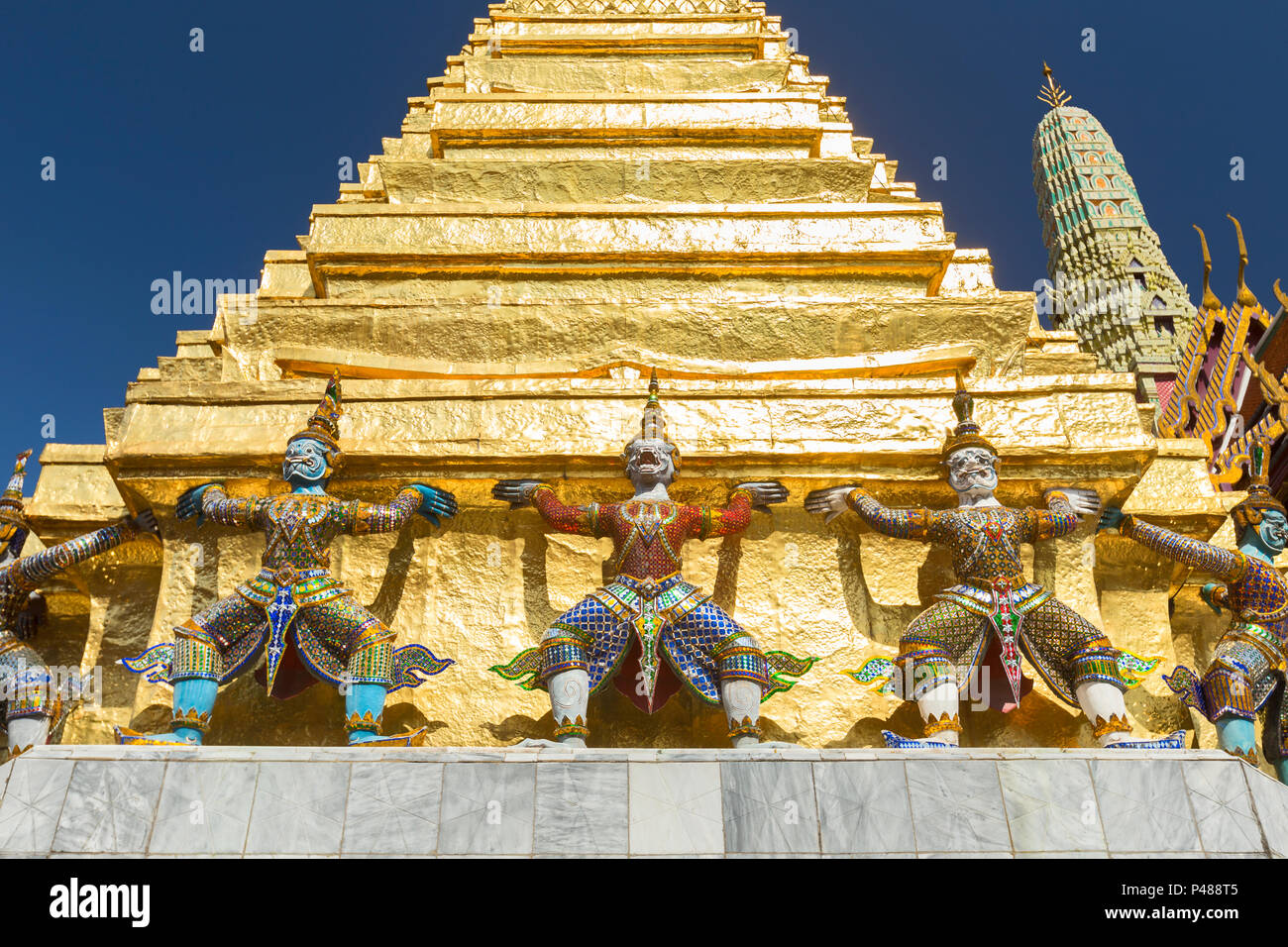 Guardian statues on the base of a golden chedi at Wat Phra Kaeo, the Royal Grand Palace, Bangkok,Thailand Stock Photo