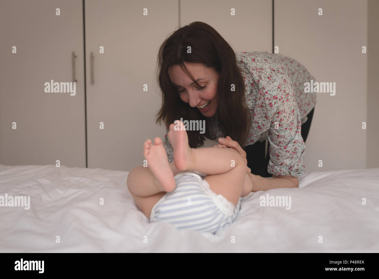 Smiling young mother playing with baby in bedroom Stock Photo