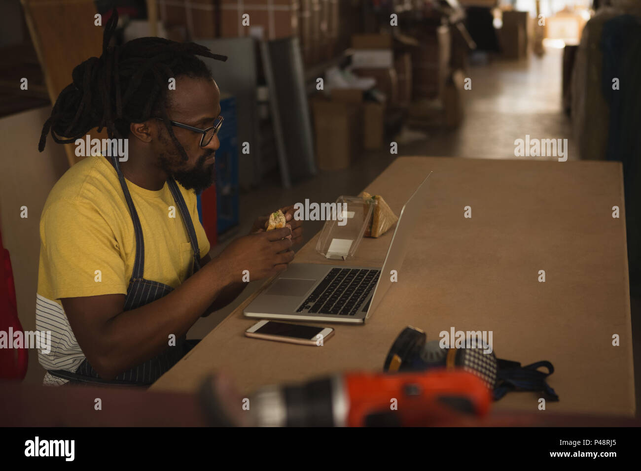 Carpenter eating sandwich while working on laptop Stock Photo