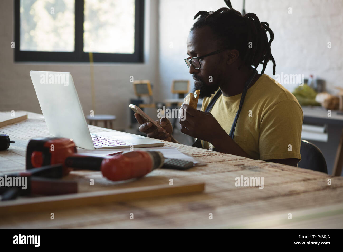 Carpenter eating sandwich while using mobile phone Stock Photo