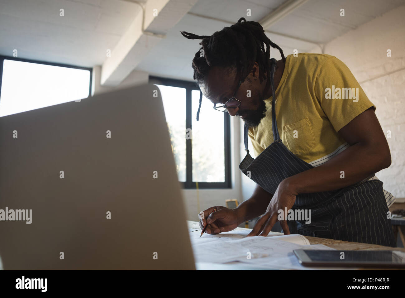 Carpenter writing in paper while using laptop at table Stock Photo
