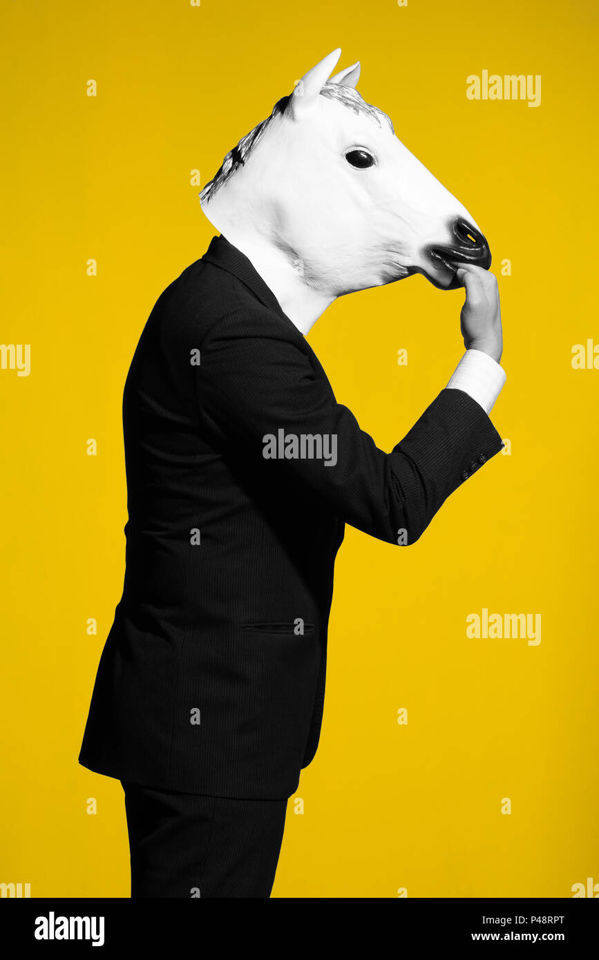 A man in a suit and a horse mask bites own hand. Conceptual business