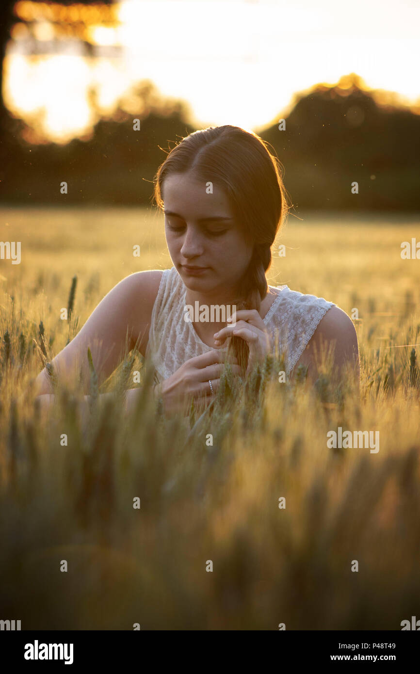 Young lady/girl sat in a golden barley field at sunset Stock Photo