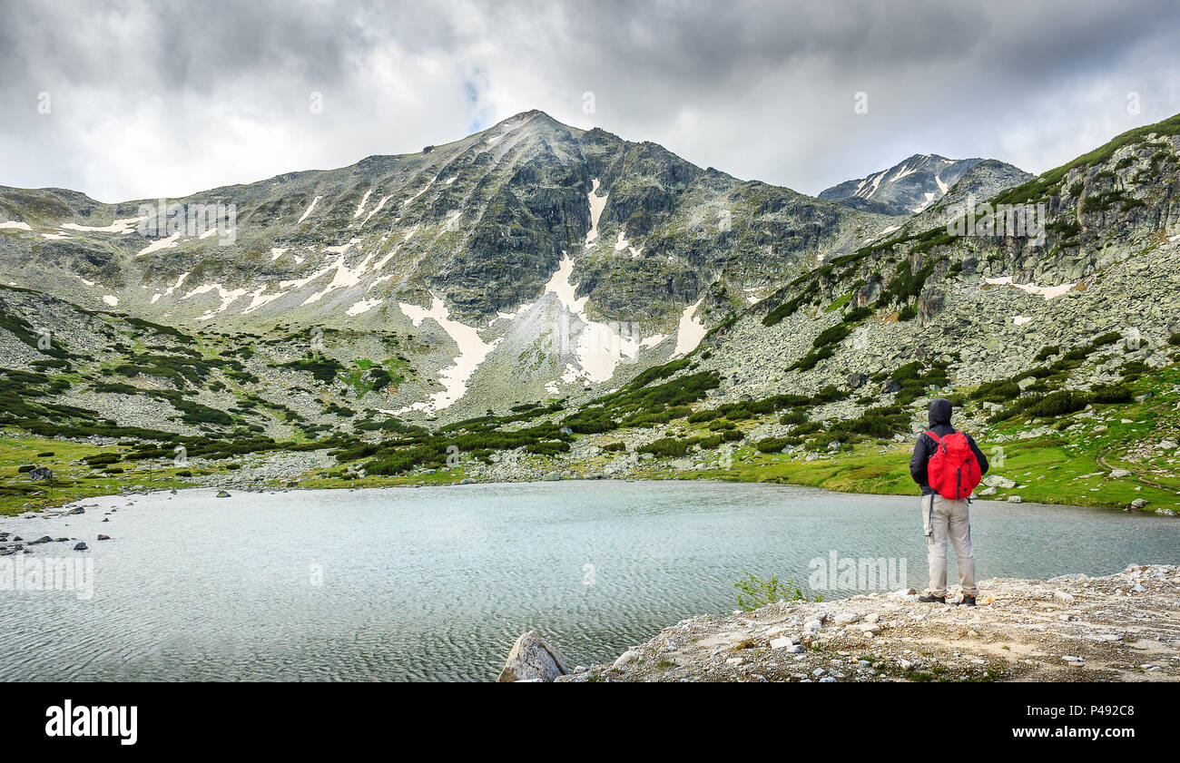 Mountain hiker looking at beautiful Rila mountain lake and snow covered Musala summit on a cloudy, dramatic day Stock Photo