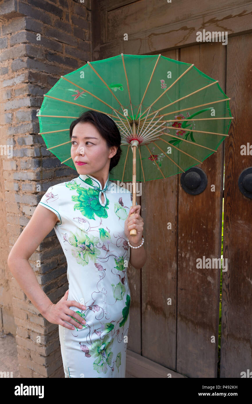Mature women in traditional tight fitting dresses carry paper parasols greet visitors, Dong E E Jiao City, Liaocheng, Shandong Province, China Stock Photo