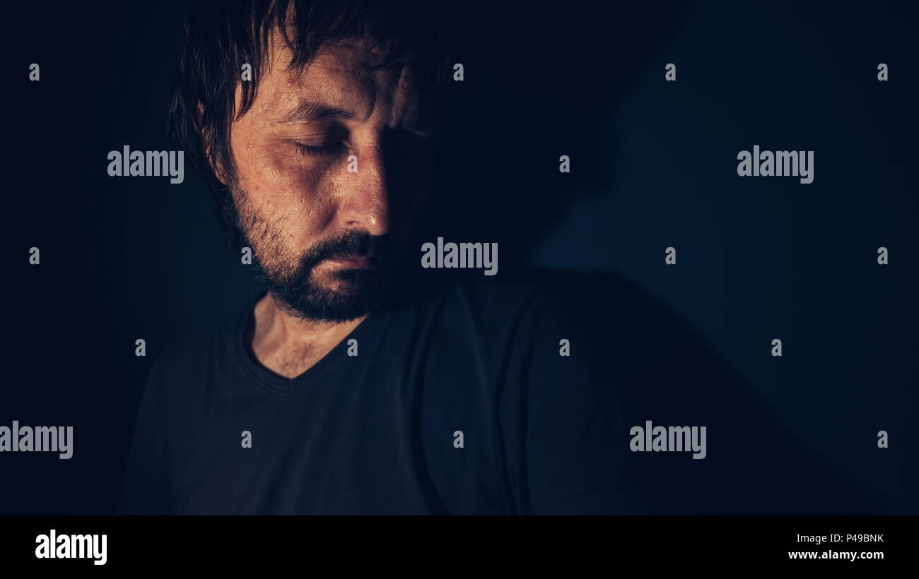 Mental health and depression concept, sad depressed man sulking in dark interior Stock Photo