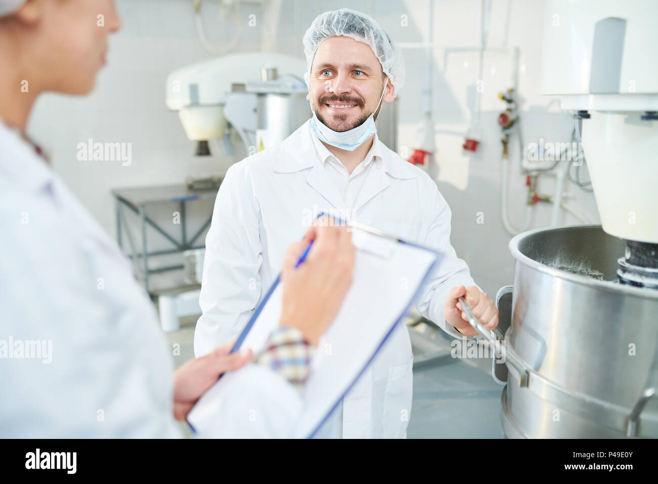 Smiling confectionery factory worker and colleague taking notes Stock