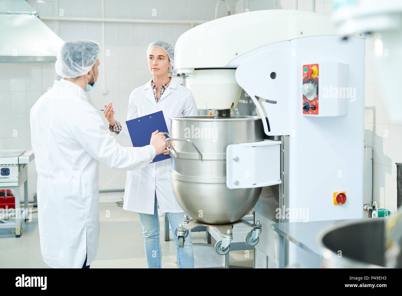 Two confectioners talking standing near machinery at factory Stock Photo