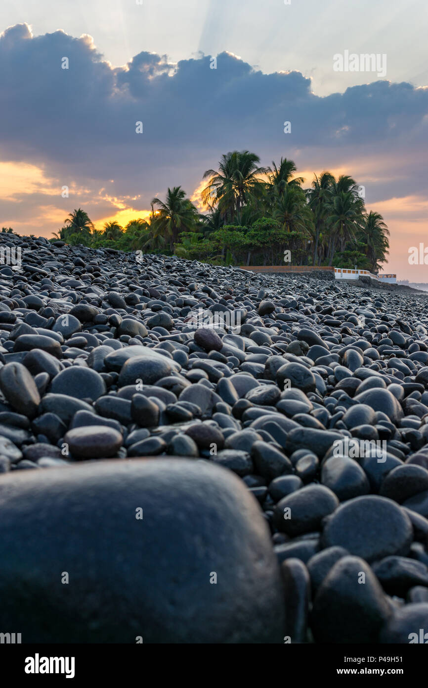 Beach at sunrise with dark rocks in the foreground - vertical. Stock Photo