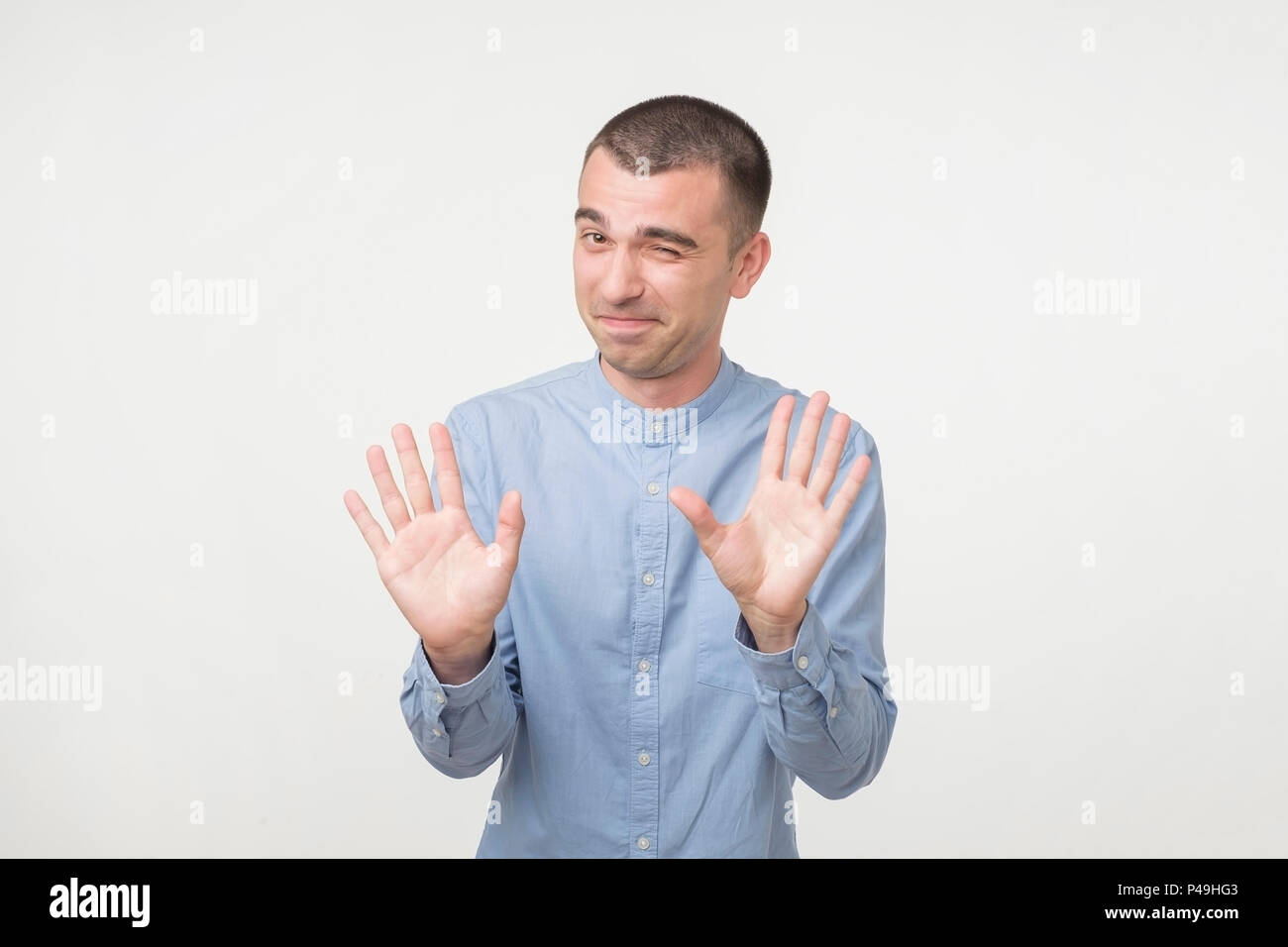 Portrait of attractive man showing hold on gesture with raised palms and smiling, standing over gray background. Wait a sec, everything happened diffe Stock Photo
