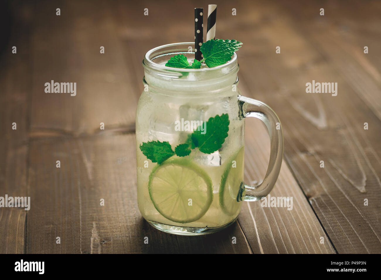 Cold Mojito Cocktail with Ice, Lemon and Mint Leaves in Mason Jar on Rustic Dark Wooden Background as Summer Concept Stock Photo