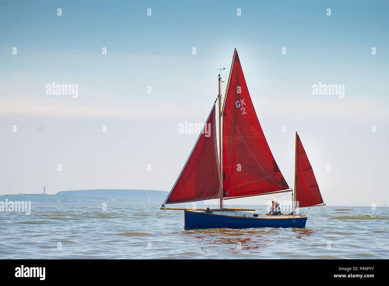 A red sailboat seen on calm sea on a warm sunny day with blue sky. Stock Photo