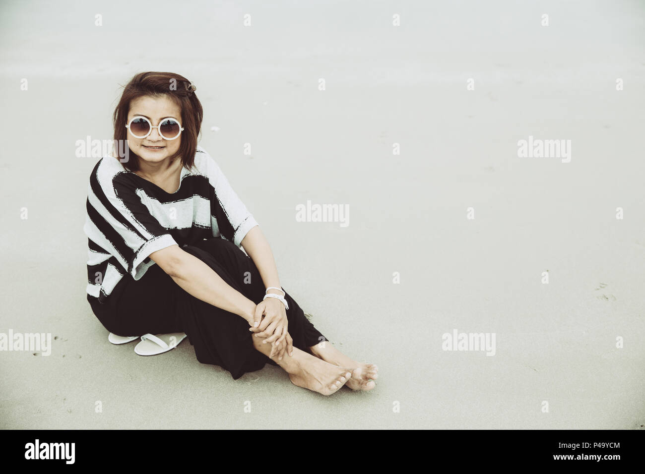 portrait asian single hipster indy women wear sunglasses lonely siting alone on the beach vintage mute color tone. Stock Photo