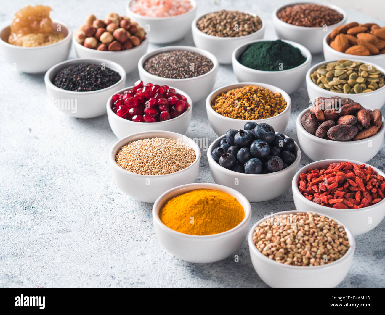 Various superfoods in smal bowl gray concrete background. Superfood as chia, spirulina, raw cocoa bean, goji, hemp, quinoa, bee pollen, black sesame, turmeric. Copy space for text. Stock Photo
