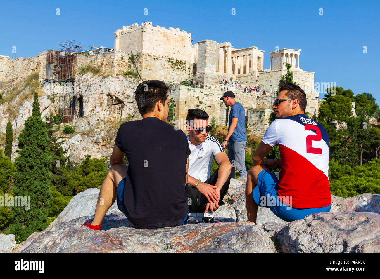 Athens, Greece - June 9, 2018: Boys seated on a rock and chatting against the Acropoilis ruins in Athens, Greece on a summer afternoon Stock Photo