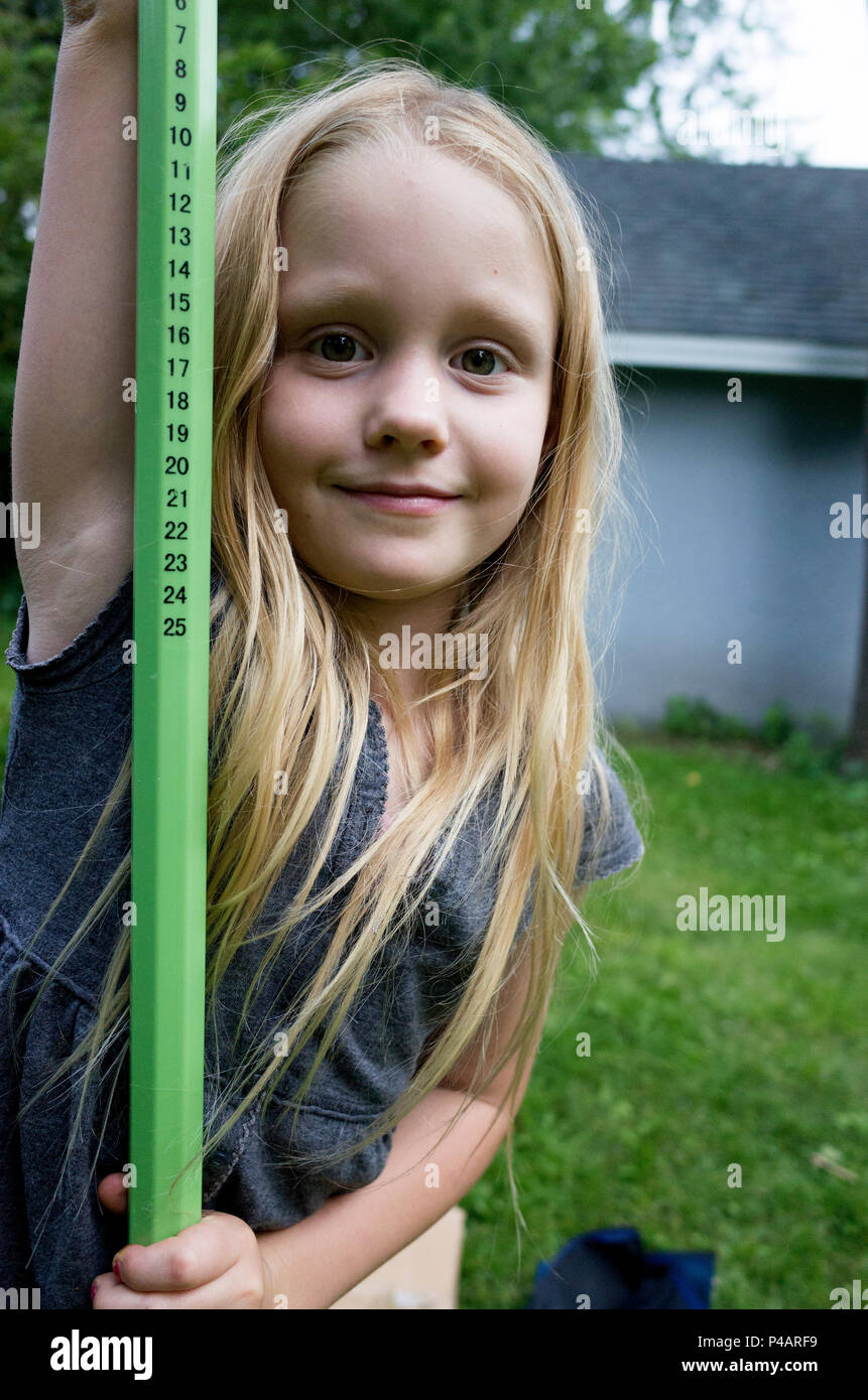 Young girl age 7 takes a break from adjusting pole for a sports net in her backyard. St Paul Minnesota MN USA Stock Photo