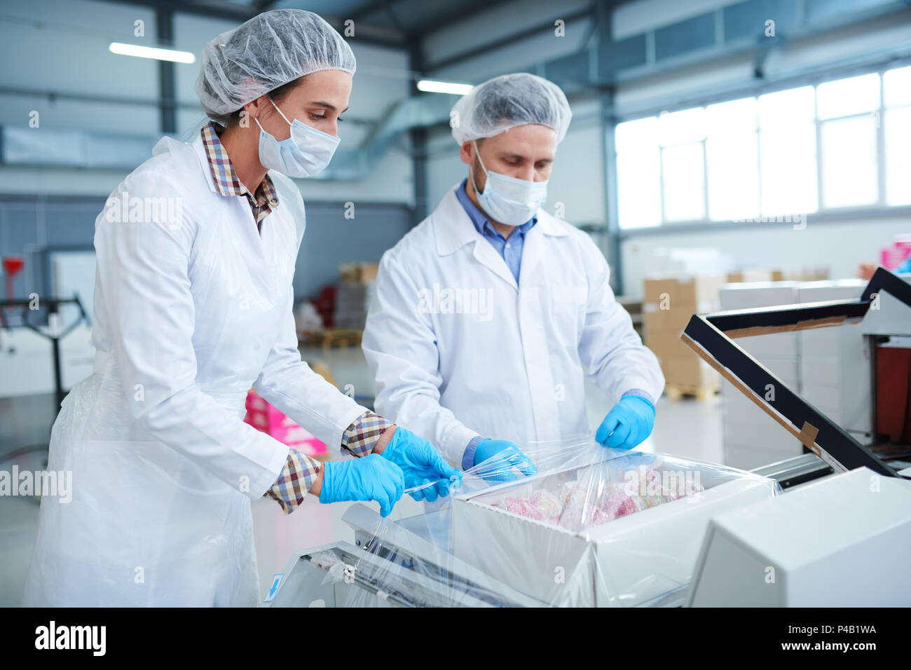 Confectionery factory workers wrapping box into packaging film Stock Photo