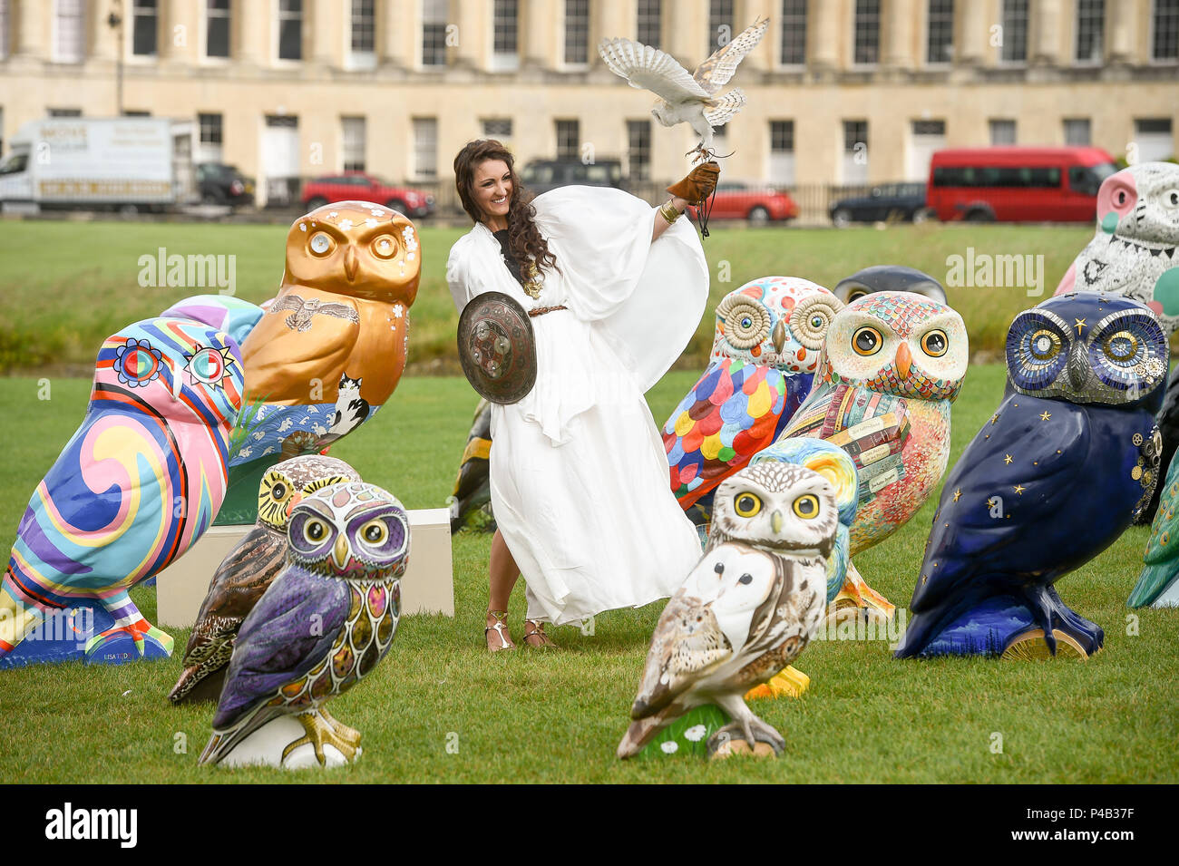 An owls sits on the hand of a woman dressed as the Roman Goddess Minerva, often referred to as the 'owl of Athena' or the 'owl of Minerva', as she stands with some of the Minerva's Owls of Bath sculptures, an art trail that takes place around the city for three months starting June 25, 2018. Stock Photo