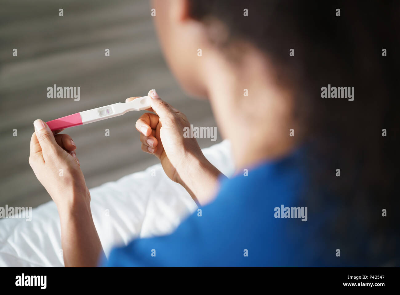 Depressed young hispanic woman with anxious feelings on bed. Black girl holding negative pregnancy test. Close-up of hands and kit Stock Photo