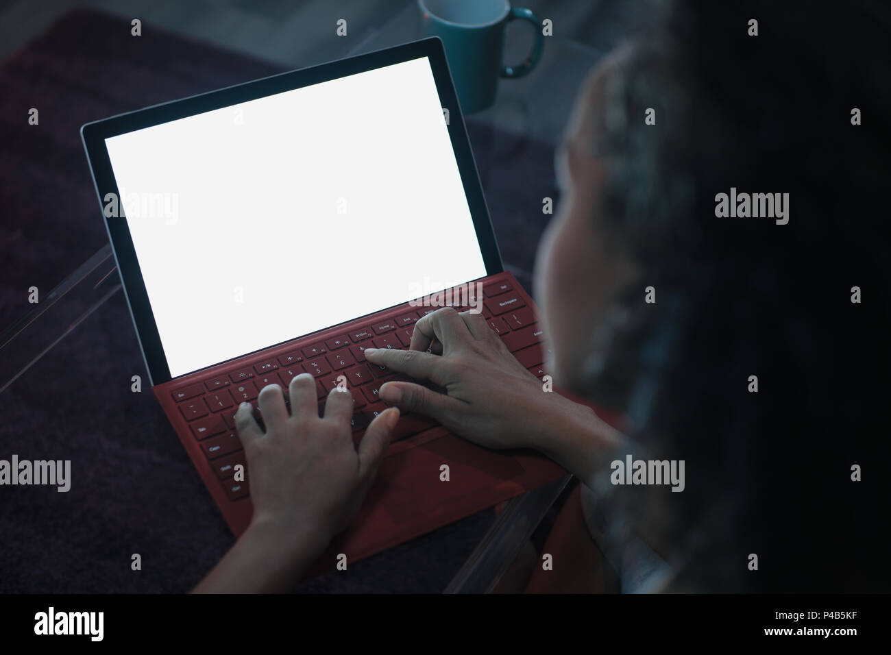 Young black woman typing on laptop computer at night. Over the shoulder shot of screen and blank monitor for mock-up Stock Photo