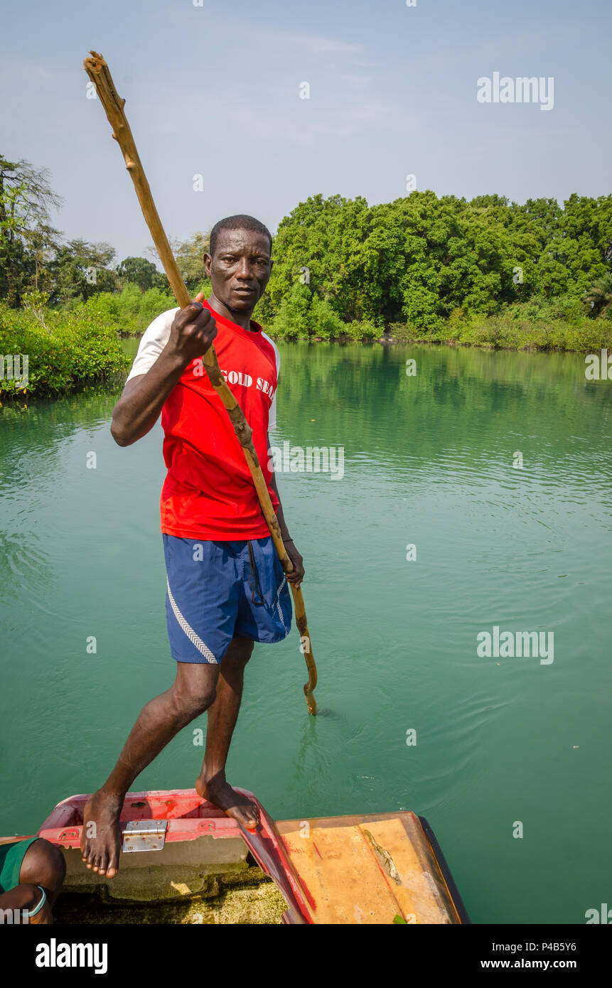 Tokeh Beach, Sierra Leone - January 06, 2014: Unidentified African man pushing simple raft on mangrove river with stick. Stock Photo