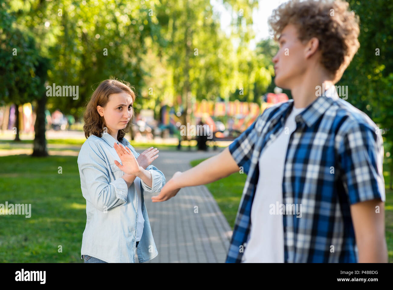 Young man in summer in a park outdoors. Tries to get acquainted with a beautiful girl. The girl gestures to show no. Unwillingness to talk. The concept of dating in the city. Stock Photo