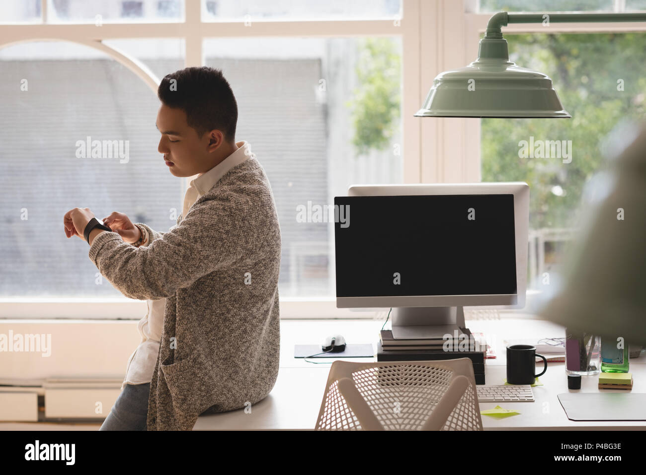 Executive sitting on desk checking time in his smartwatch Stock Photo
