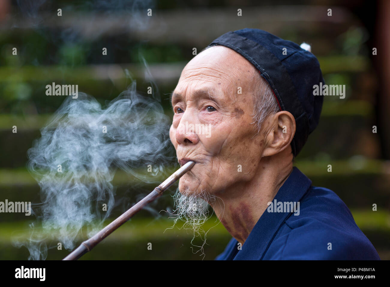 Ethnic minority man smokes traditional long pipe, Hsui ethnic minority village Water Flower, Libo, Guizhou Province, China Stock Photo