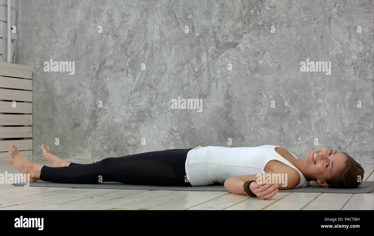 Attractive young woman working out at home, doing yoga exercise on blue mat, lying in Shavasana Corpse or Dead Body Posture , resting after practice, meditating, breathing Stock Photo