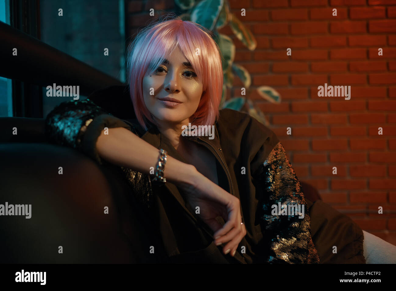 Girl with pink hair sitting relaxed on a leather sofa Stock Photo - Alamy