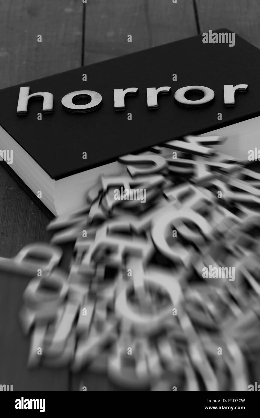 Book novel with the word horror and blurred letters coming out of the pages on a wood background Stock Photo
