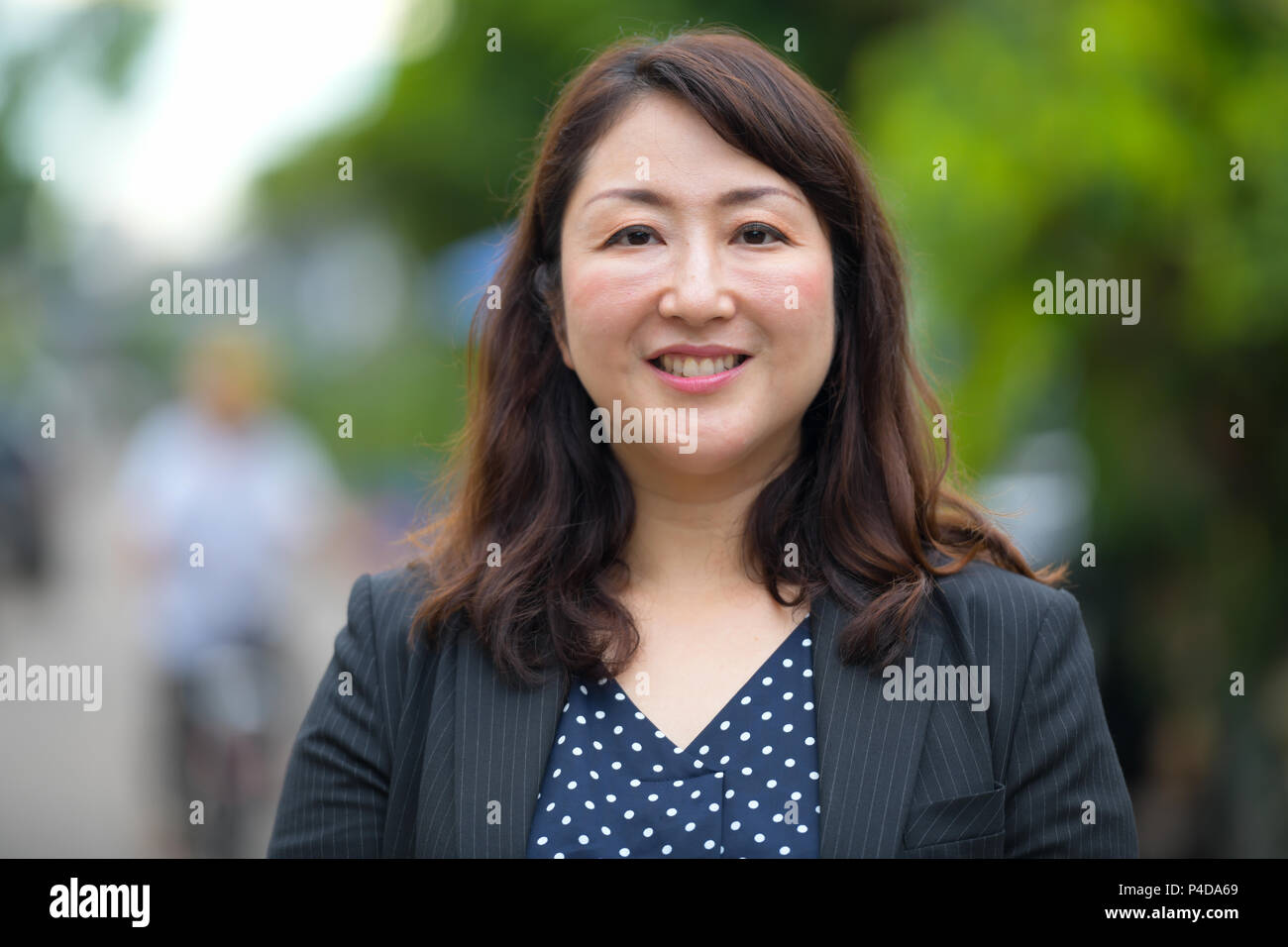 Mature happy beautiful Asian businesswoman smiling in the streets outdoors Stock Photo