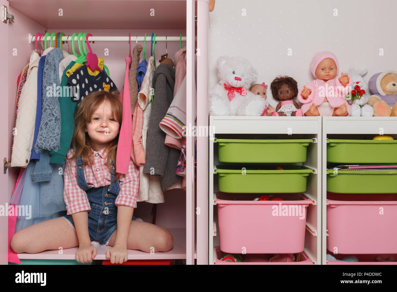 A little girl is sitting in a closet with a children's department. Storage system for children's things and toys Stock Photo