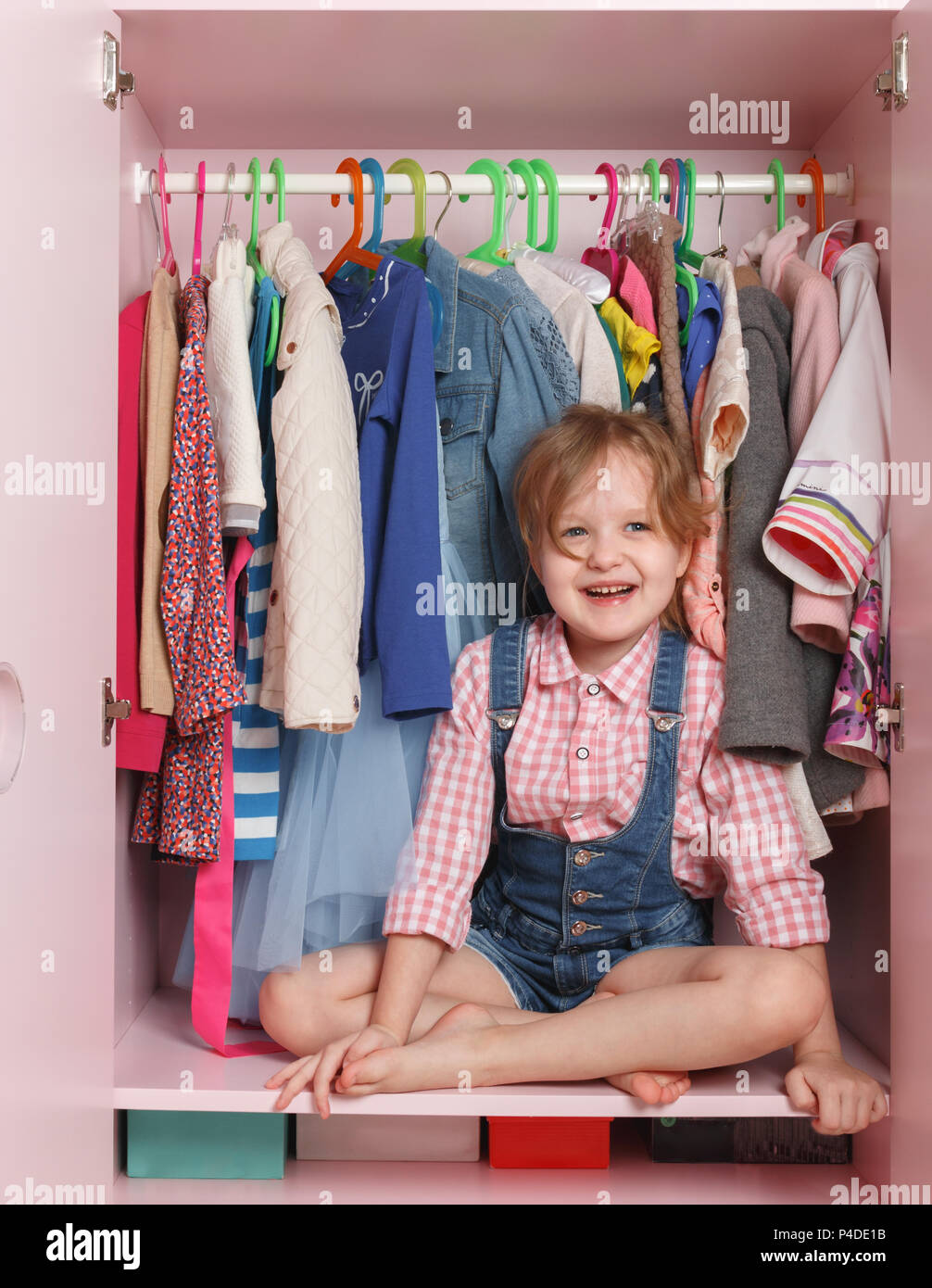 A little girl is sitting in a closet with a children's department. Storage system for children's things Stock Photo