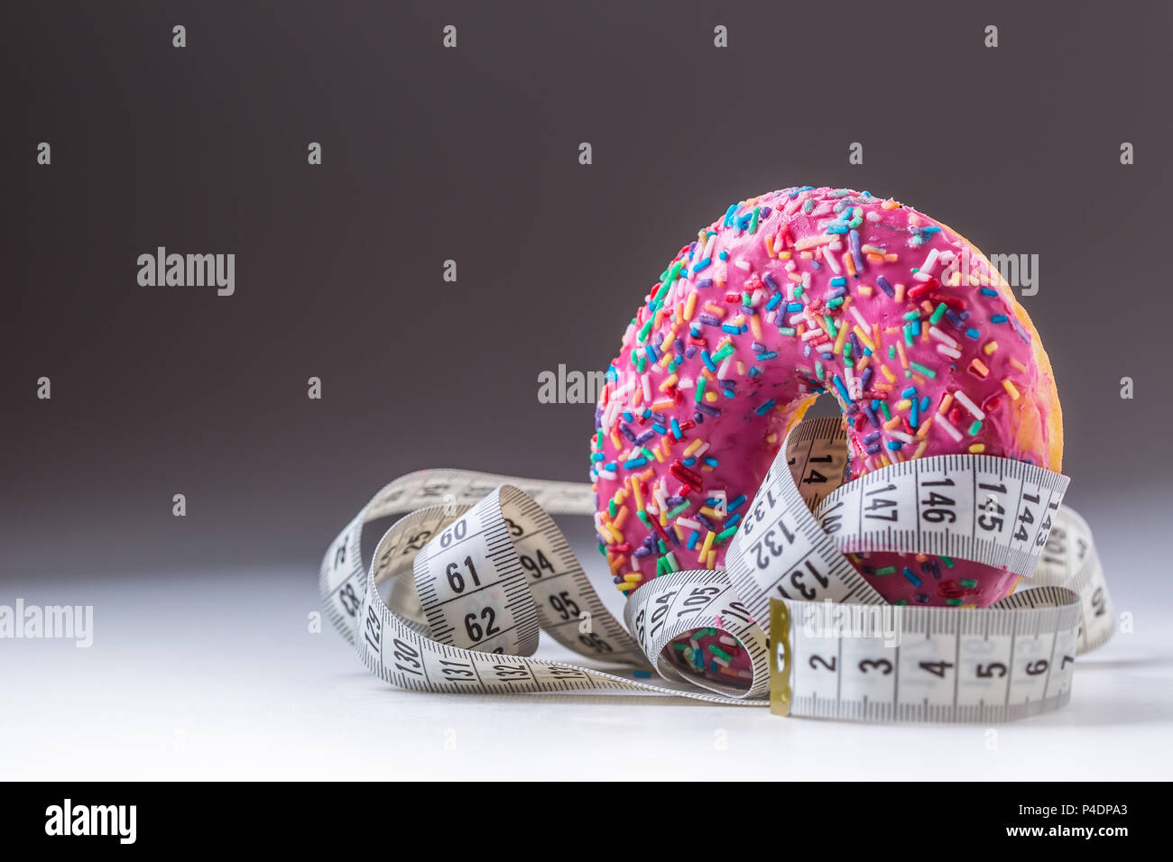Close-up pink frosted donut with white tailor measure tape. Stock Photo