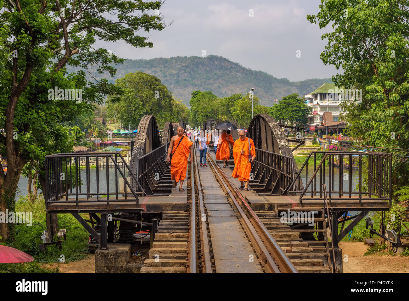 Buddhist monks walk on the bridge over the river Kwai in Thailand Stock Photo