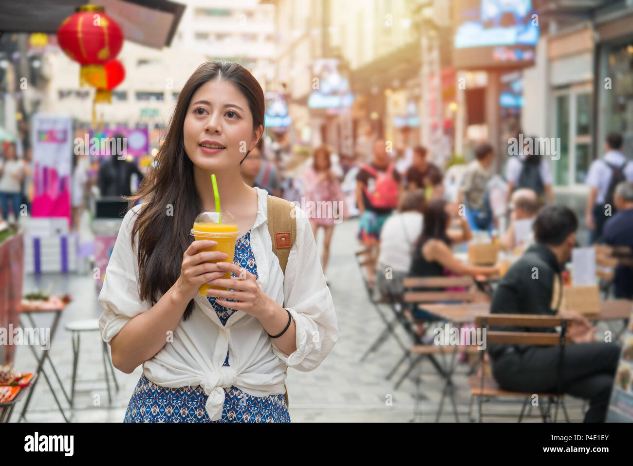 Asian woman holding a cup of mango juice and walking in the street market shopping in the market at the same time. Stock Photo