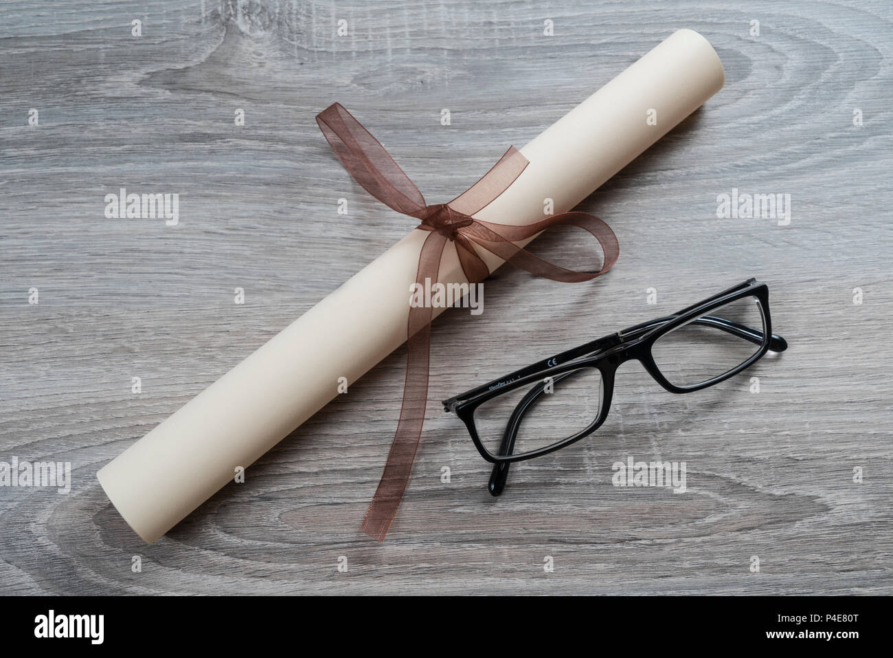 a diploma rolled up and tied with a red ribbon on the table with a pair of glasses Stock Photo