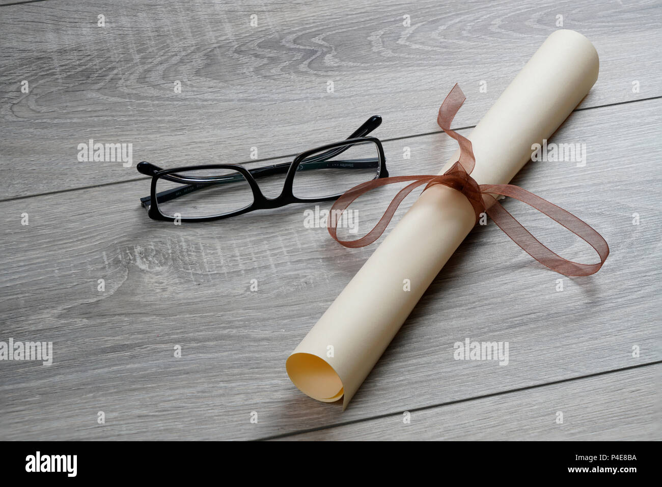 a diploma rolled up and tied with a red ribbon on the table with a pair of glasses Stock Photo