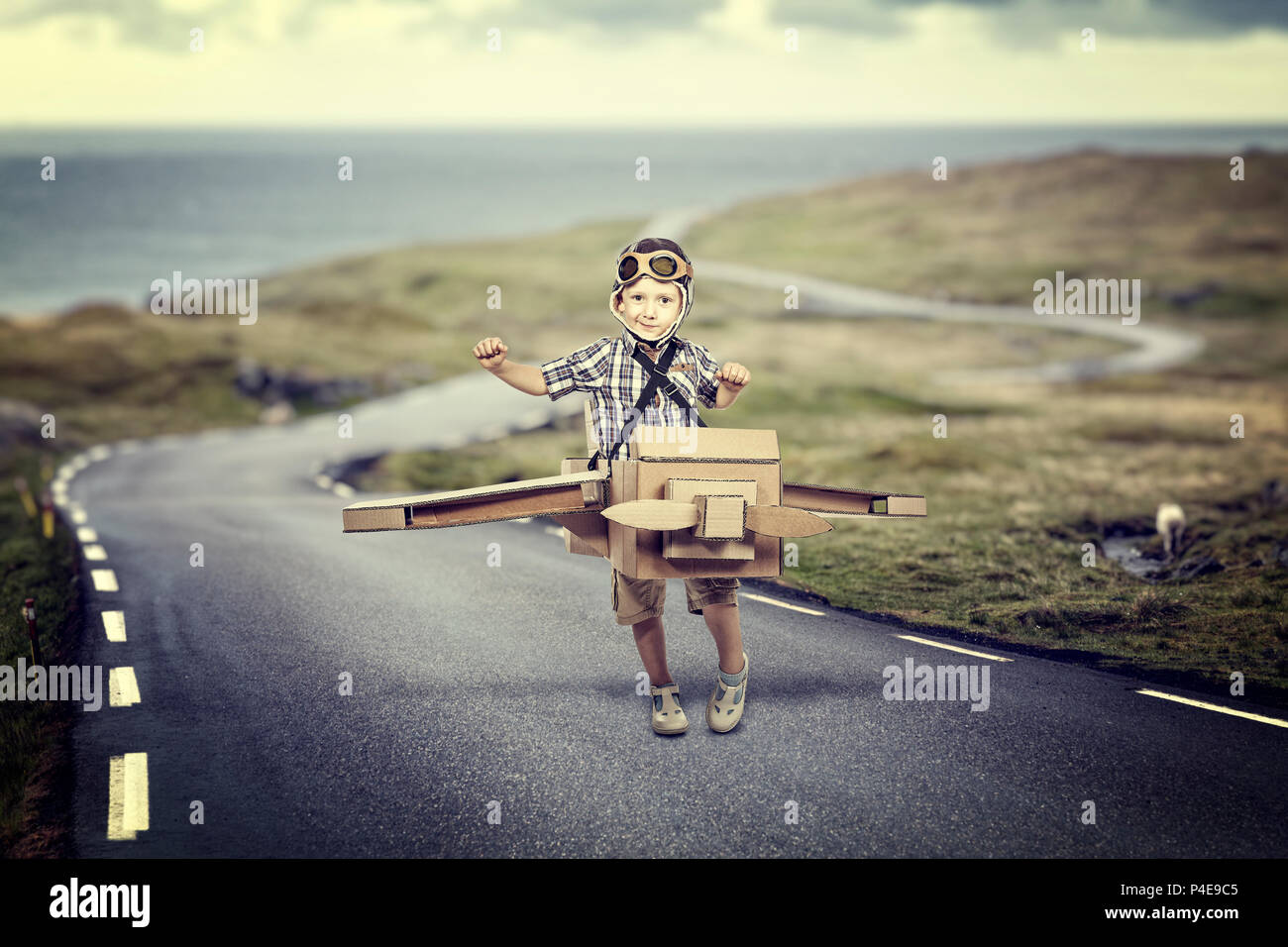 Kid play to be a pilot with cardboard airplane on lonely road a Stock Photo