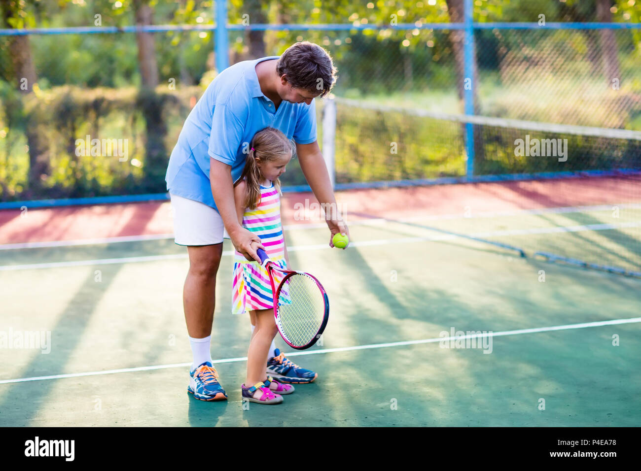 Father and daughter playing tennis on outdoor court. Family with tennis