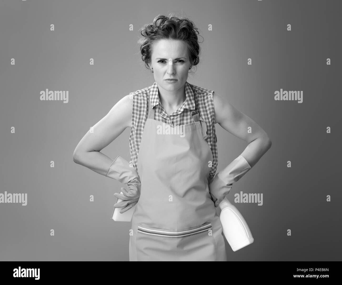 Big cleaning time. Tense young woman in a apron with cleaning sponge and detergent isolated on Stock Photo