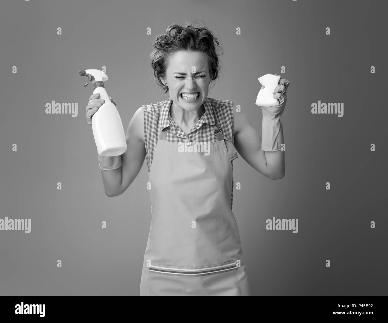 Big cleaning time. angry modern woman in a apron with kitchen sponge and a bottle of detergent isolated on Stock Photo