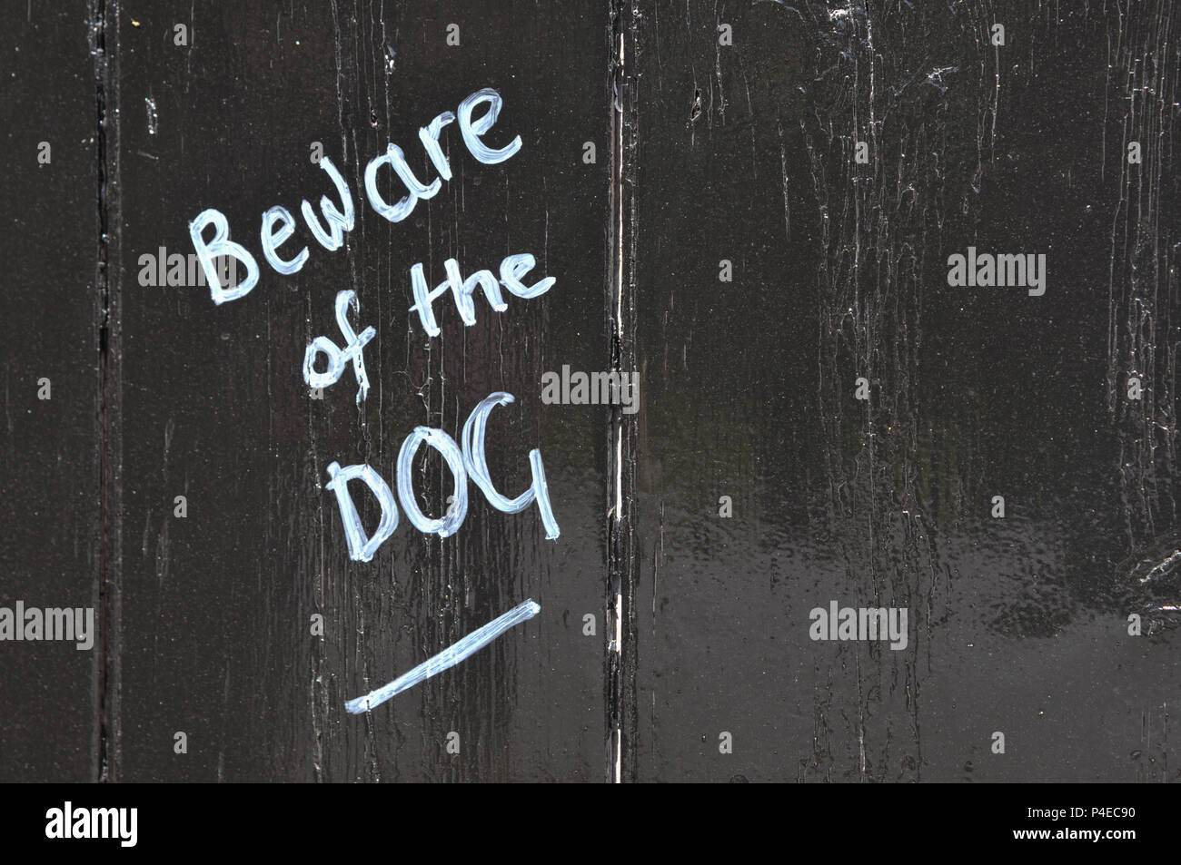Beware of the dog chalk writing on a black painted wooden fence Stock Photo
