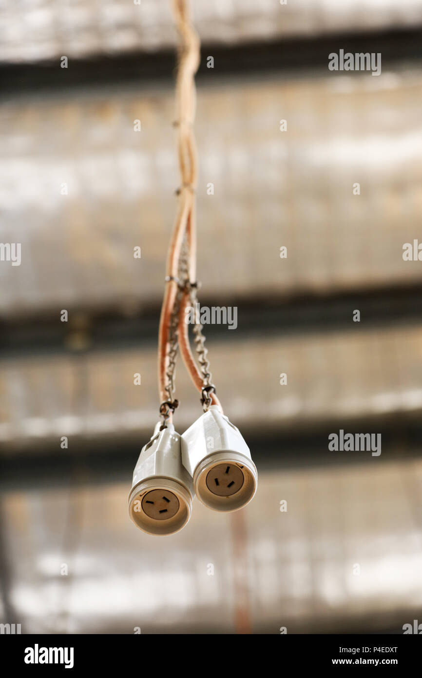a pair of 3 pin power socket cord cable wire hanging from a factory ceiling roof. power supply. electrical cabling into a workshop. Stock Photo