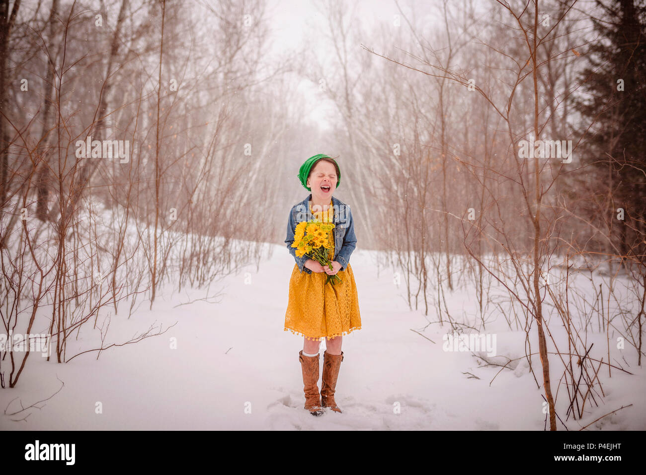 Smiling girl standing in the snow holding a bunch of yellow flowers Stock Photo