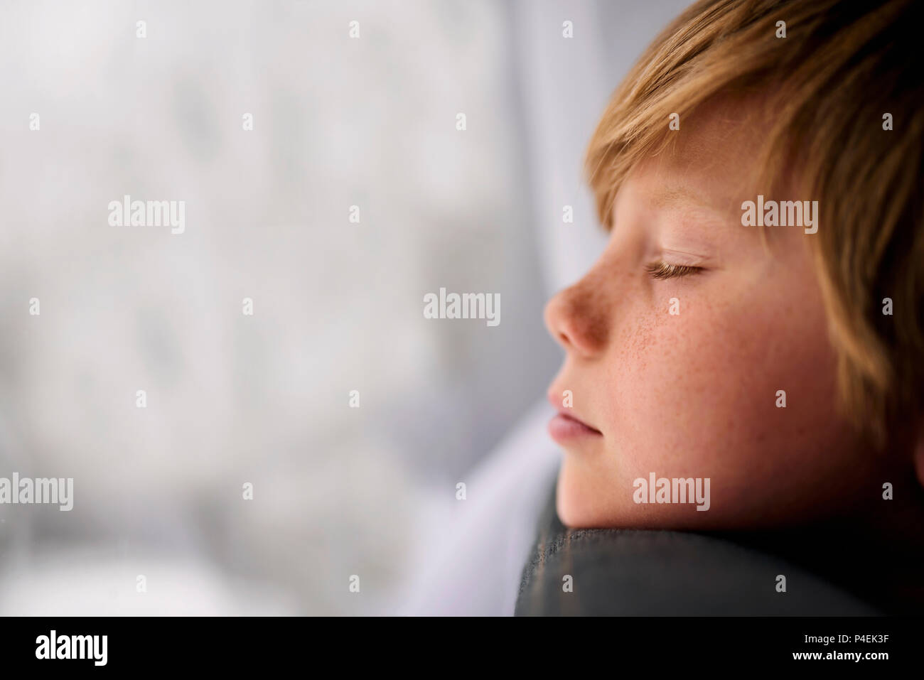 Boy standing by a window with his eyes closed Stock Photo