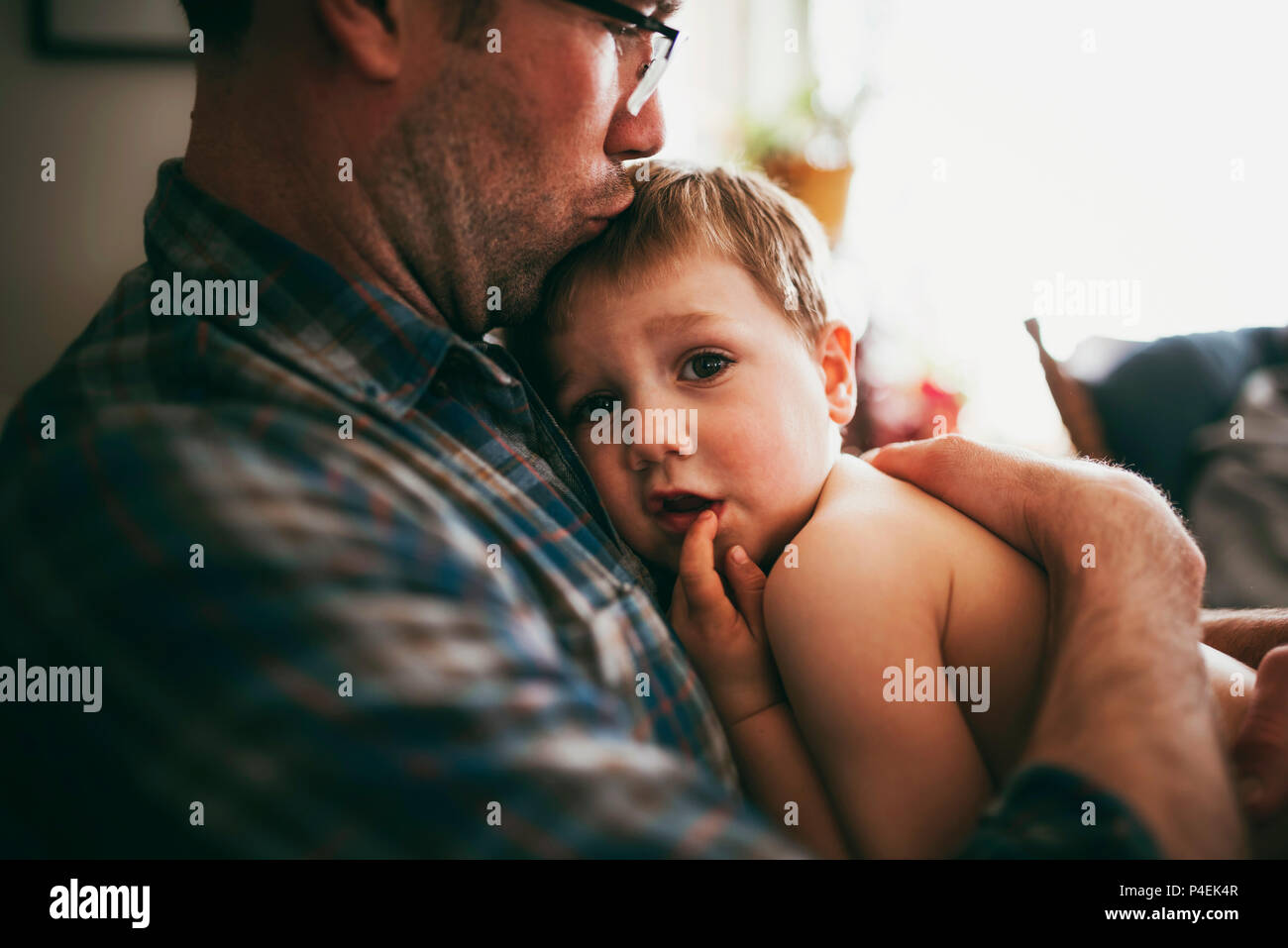 Father sitting on couch cuddling his son and kissing him on the head Stock Photo